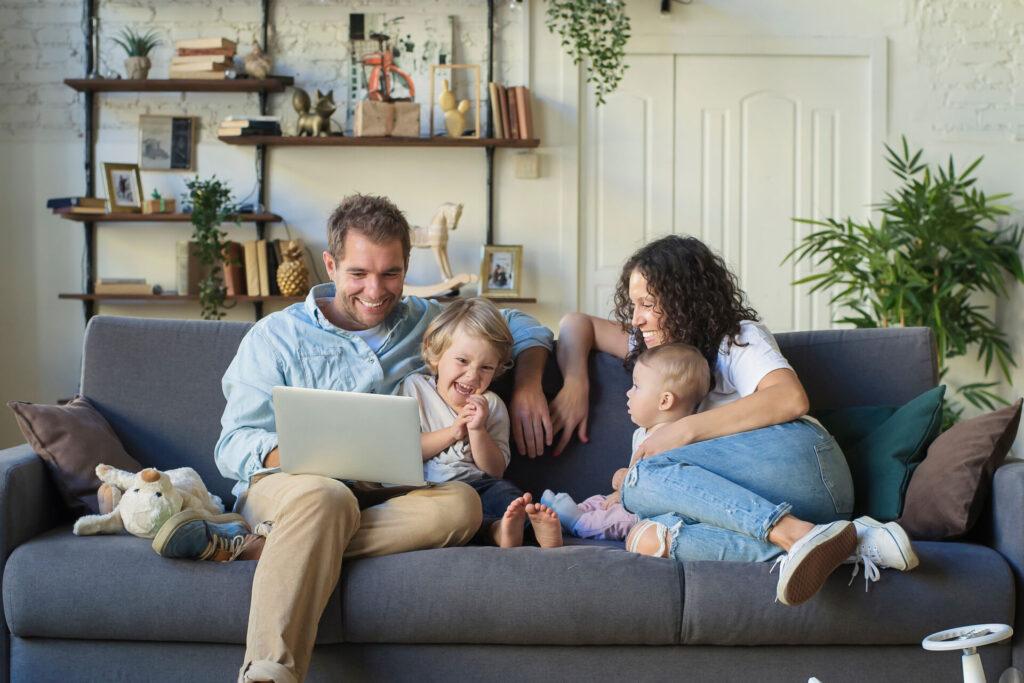 A family sitting on a couch, smiling at a laptop