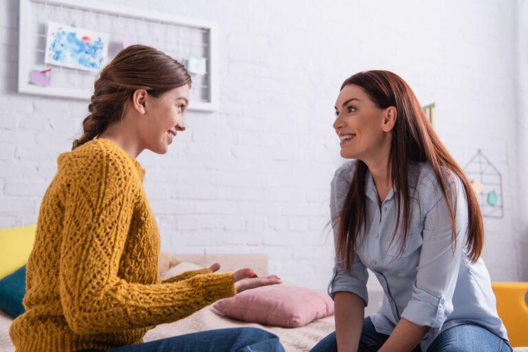 Two women sitting facing each other and looking happy