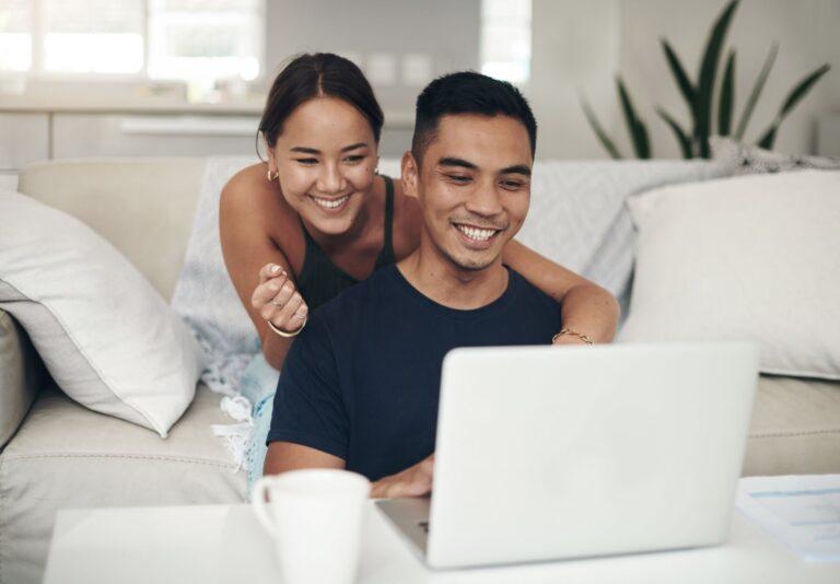 Happy looking couple sitting on sofa looking at laptop screen