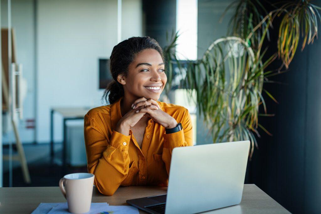Business woman sitting at an office desk and smiling while thinking